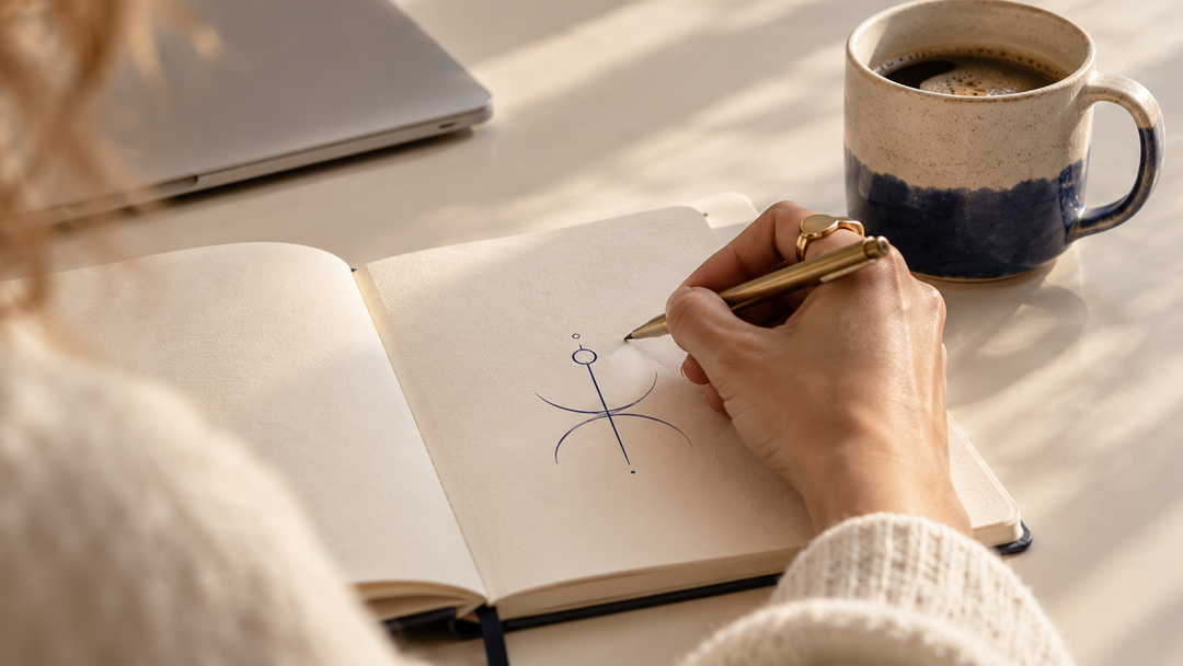 Hand drawing a sigil in a notebook next to a coffee mug